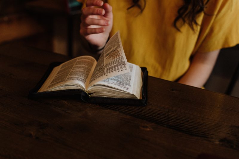 person reading Bible on top of brown wooden table