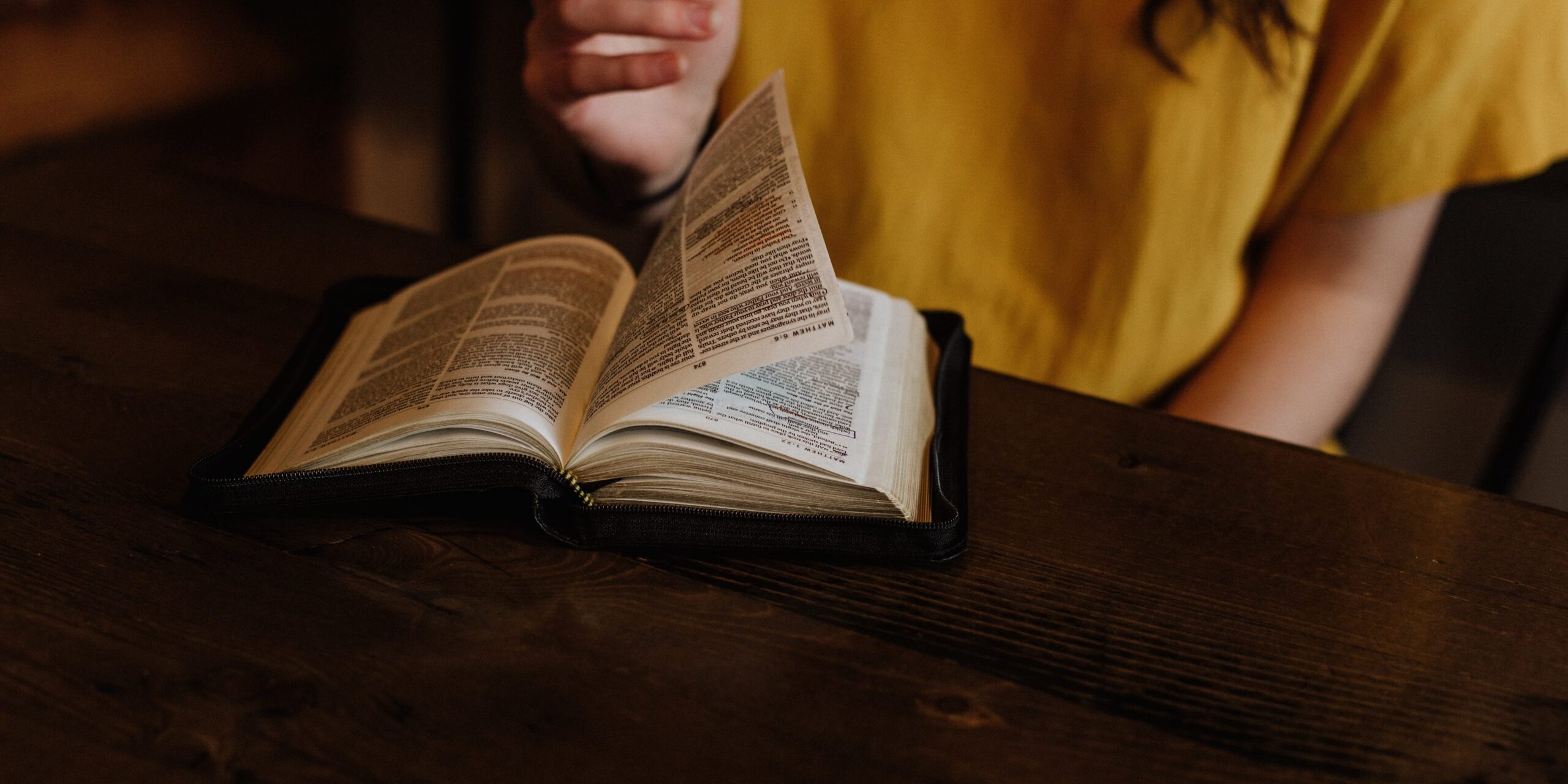 person reading Bible on top of brown wooden table